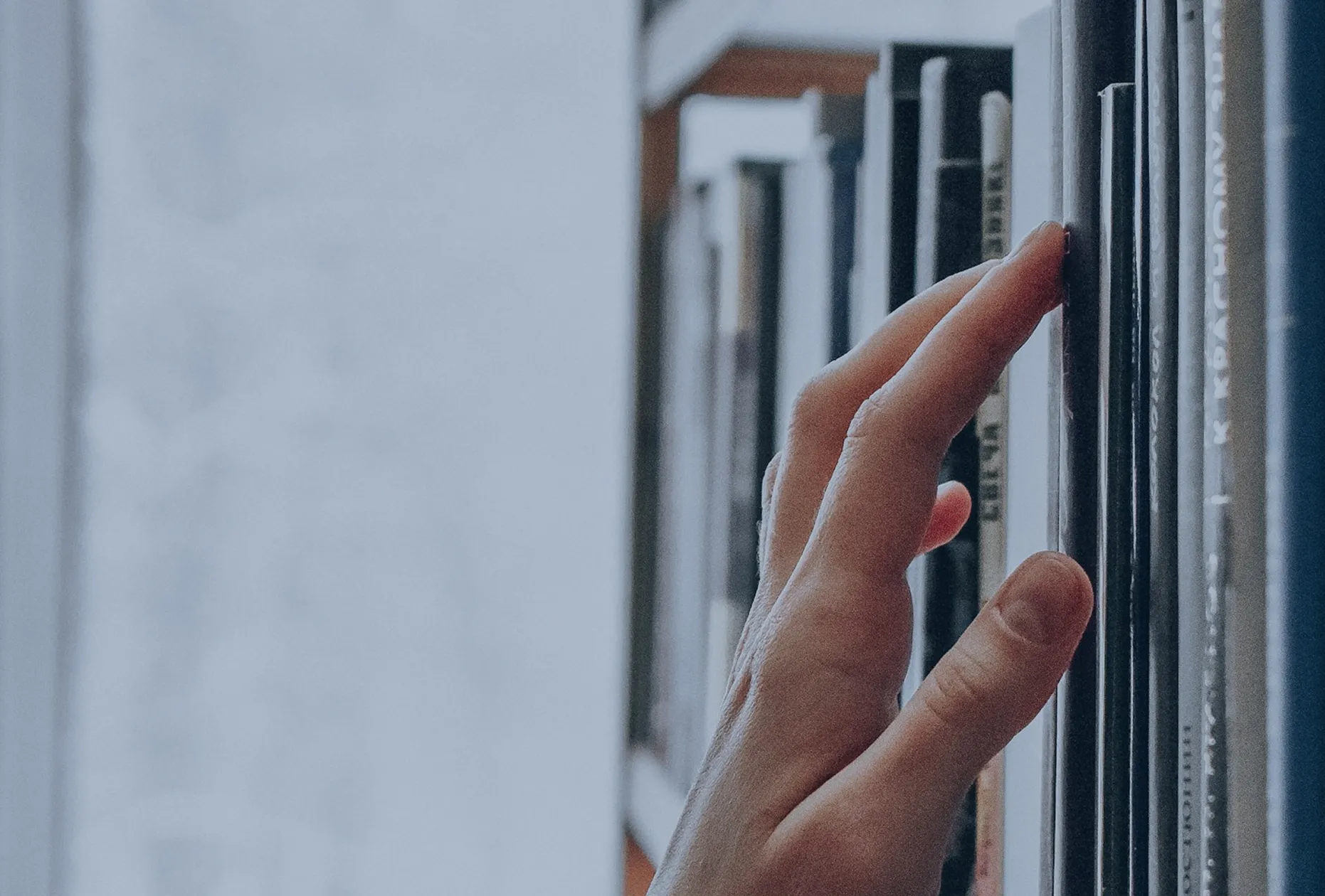 Eine Hand berührt einen Buchrücken in einem Bücherregal.